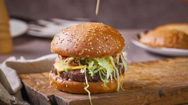 Şef, ev mutfağında lezzetli bir biftek burgeri hazırlıyor, ahşap bir tahtanın üzerinde, yemek yakın plan.