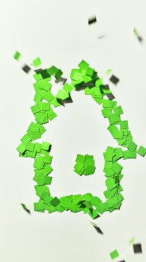 Yeşil renkli kağıt parçalarından yapılmış ev sembolü uçup gidiyor. Beyaz arka plan, yeşil ev kavramı