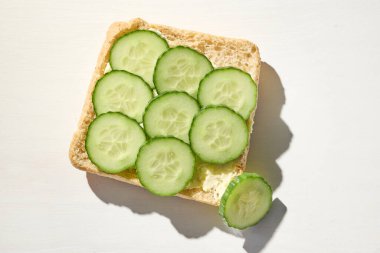 Krem şantili ekmek dilimi ve sağlıklı kahvaltı için salatalık, güneşli mutfak masasında, üst manzara.