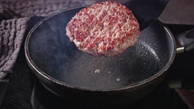Şef, kızartılmış biftekli burgeri sıcak tavada çevirin, yemek yakın plan.