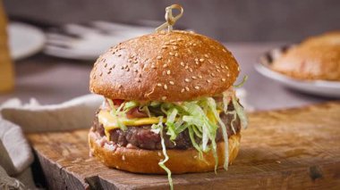 Şef, ev mutfağında lezzetli bir biftek burgeri hazırlıyor, ahşap bir tahtanın üzerinde, yemek yakın plan.