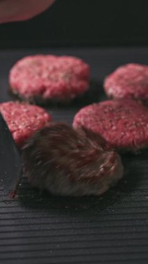 Aşçı, kıymalı burger köfteleri, sıcak, siyah ızgara yüzeyi pişirir.