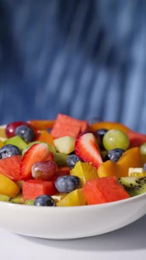 Bir kase taze meyve salatası mavi arka planda dönüyor, yiyecek yakın plan, sağlıklı beslenme
