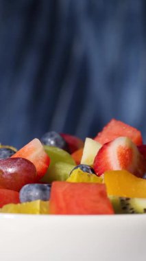 Bir kase taze meyve salatası mavi arka planda dönüyor, yiyecek yakın plan, sağlıklı beslenme
