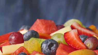 Bir kase taze meyve salatası mavi arka planda dönüyor, yiyecek yakın plan, sağlıklı beslenme