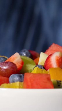 Bir kase taze meyve salatası mavi arka planda dönüyor, yiyecek yakın plan, sağlıklı beslenme