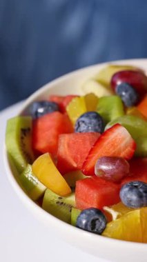 Bir kase taze meyve salatası mavi arka planda dönüyor, yiyecek yakın plan, sağlıklı beslenme