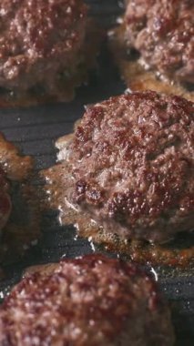 Kıymalı biftek köfteleri sıcak, siyah elektrikli ızgara yüzeyinde pişiyor.