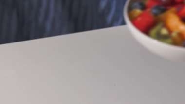 Taze meyve salatasıyla dolu beyaz bir kase sağlıklı bir yemek için insan eliyle masaya konur.