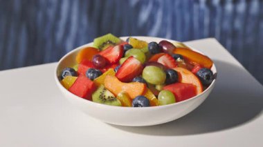 Mavi arka planda bir kase taze meyve salatası, yakın plan yemek, sağlıklı beslenme, çatallı el bir parça çilek al.