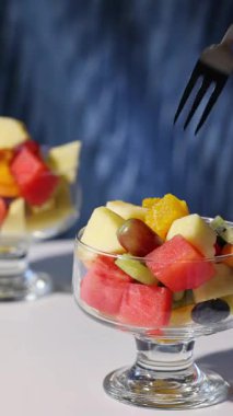 Mavi arka planda bir kase taze meyve salatası, yakın planda yemek, sağlıklı beslenme, çatallı el bir parça portakal al.