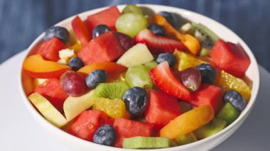 Bir kase taze meyve salatası mavi arka planda dönüyor, yiyecek yakın plan, sağlıklı beslenme