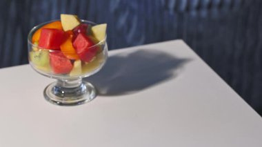 Taze meyve salatasıyla dolu bir cam kase sağlıklı bir yemek için insan eliyle masaya konur.