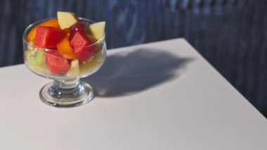 Taze meyve salatasıyla dolu bir cam kase, sağlıklı bir yemek için insan eliyle masaya konur.