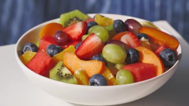 Taze meyve salatasıyla dolu beyaz kâse insan eliyle masadan kaldırıldı, sağlıklı yemek zoom 'u.