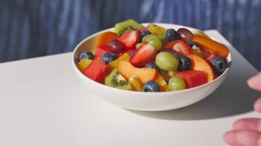 Taze meyve salatasıyla dolu beyaz kâse insan eliyle masadan kaldırıldı, sağlıklı yemek. 