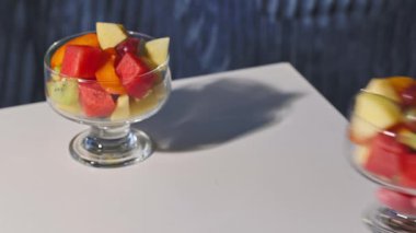 Taze meyve salatasıyla dolu bir cam kase, sağlıklı bir yemek için insan eliyle masaya konur.