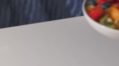 Taze meyve salatasıyla dolu beyaz bir kase, sağlıklı bir yemek için insan eliyle masaya konur.