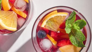 Kırmızı sangria bardaklarına yakın çekim, taze meyve parçaları, buz ve dut, nane yaprağı ile süslenmiş, üst manzara, güneşli arka plan
