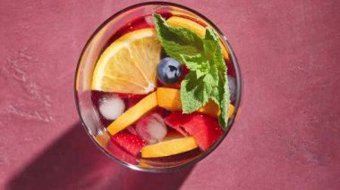 Kırmızı sangria bardağına yakın çekim. Taze meyve parçaları, buz ve böğürtlen. Nane yaprağı ile süslenmiş.