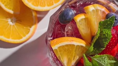 Kırmızı sangria bardağının yakın plan görüntüsü taze meyve parçaları, buz ve böğürtlen, nane yaprağı ile süslenmiş, güneşli ışık arka planında,