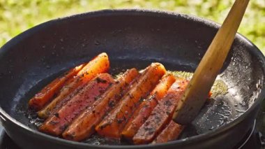 Açık hava yemekleri. Haşlanmış havuçları sıcak tavada pişirmek yağlı, bahçede lezzetli yemekler pişirmek için yakın plan, açık hava.