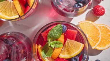Kırmızı sangria bardaklarına yakın çekim, taze meyve parçaları, buz ve dut, nane yaprağı ile süslenmiş, üst manzara, güneşli arka plan