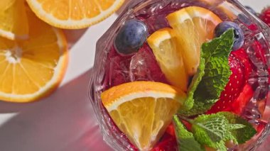 Kırmızı sangria bardağının yakın plan görüntüsü taze meyve parçaları, buz ve böğürtlen, nane yaprağı ile süslenmiş, güneşli ışık arka planında,