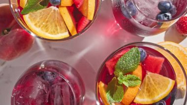 Kırmızı sangria bardaklarına yakın çekim, taze meyve parçaları, buz ve dut, nane yaprağı ile süslenmiş, üst manzara, güneşli arka plan