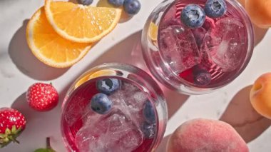 Kırmızı sangria bardağının yakın plan görüntüsü. Taze meyve parçaları, buz ve böğürtlenler. Güneşli arka planda üst manzara.