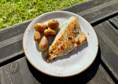 Taze ızgara balık fileto ve patates tabağı güneşli ahşap arka planda.