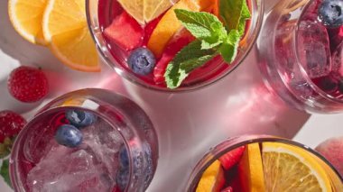 Nane yaprağıyla süslenmiş taze meyve parçaları, buz ve böğürtlen içeren dönen kırmızı sangria bardaklarının yakın plan fotoğrafı.