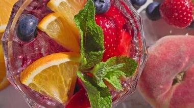 Kırmızı sangria bardağının yakın plan görüntüsü taze meyve parçaları, buz ve böğürtlen, nane yaprağı ile süslenmiş, güneşli ışık arka planında,