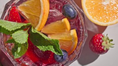 Kırmızı sangria bardağının yakın plan görüntüsü taze meyve parçaları, buz ve böğürtlen, nane yaprağı ile süslenmiş, güneşli ışık arka planında,