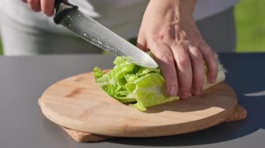Şef sağlıklı bir salata hazırlamak için tahtaya taze yeşil marul yaprakları kesiyor. Açık hava yemekleri, yakın mesafe yemekleri.