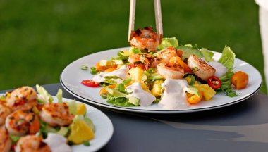 Şef taze hazırlanmış sağlıklı sebze salatasının porsiyonuna ızgara karides koydu. Açık hava yemekleri, yakın plan yemekler.