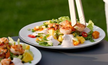 Şef taze hazırlanmış sağlıklı sebze salatasının porsiyonuna ızgara karides koydu. Açık hava yemekleri, yakın plan yemekler.