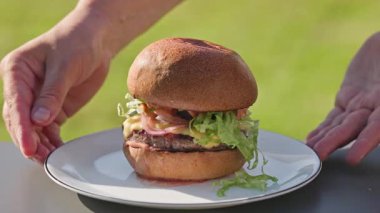 Pişirilmiş taze ızgara sulu burger, erimiş peynir ve soğanlı ekmek, soslu ekmek, güneşli bahçede yemek, açık havada pişirme.