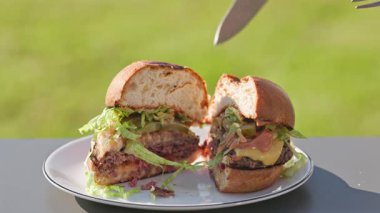 Pişirilmiş taze ızgara sulu burger, erimiş peynir ve soğanlı ekmek, soslu ekmek, güneşli bahçede yemek, açık havada pişirme.