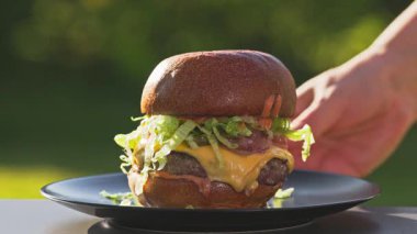 Aşçı, taze ızgara burgeri erimiş peynirli ve soğanlı ekmeği, güneşli bahçede soslu ekmeği, yemekleri yakın plan, açık havada pişirmeyi kaldırır.