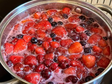 Bir tencerede çeşitli kırmızı böğürtlenler kaynıyor. Ev yapımı reçel yapma süreci, yakın çekim yiyecekler.