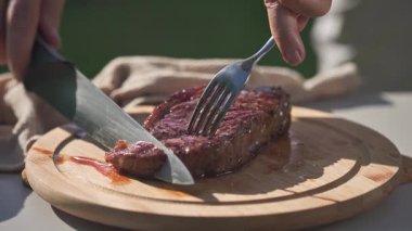 Bir aşçı taze ızgara biftek kesiyor arka bahçedeki ahşap kesme tahtası, yakın plan yemek, açık hava yemekleri.
