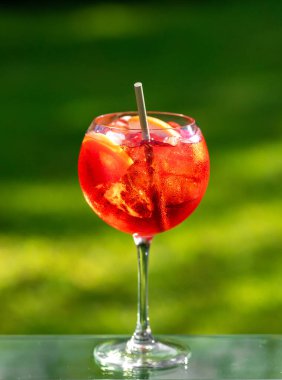 Yeşil bahçe arka planında buz ve greyfurt parçaları olan klasik kırmızı spritz kokteyli.