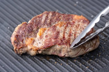 Sıcak elektrikli ızgara yüzeyinde tuzlu ve biberli taze ızgara biftek.