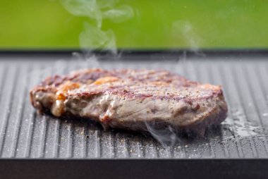 Sıcak elektrikli ızgara yüzeyinde tuzlu ve biberli taze ızgara biftek.