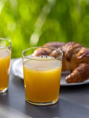 Güneşli masada iki bardak portakal suyu ve kruvasan, seçici odaklanma.