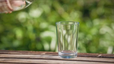 Yeşil yaz bahçesi arka planında, ahşap masada, cam üzerine dökülen taze maden suyu. Yiyecek ve içecek yakın mesafede.