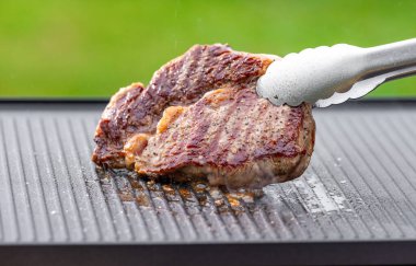 Sıcak elektrikli ızgara yüzeyinde tuzlu ve biberli taze ızgara biftek.