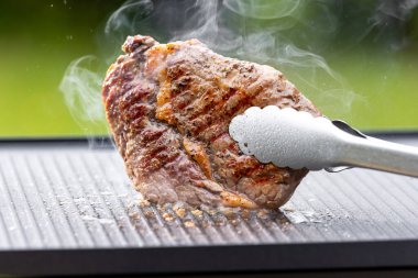 Sıcak elektrikli ızgara yüzeyinde tuzlu ve biberli taze ızgara biftek.