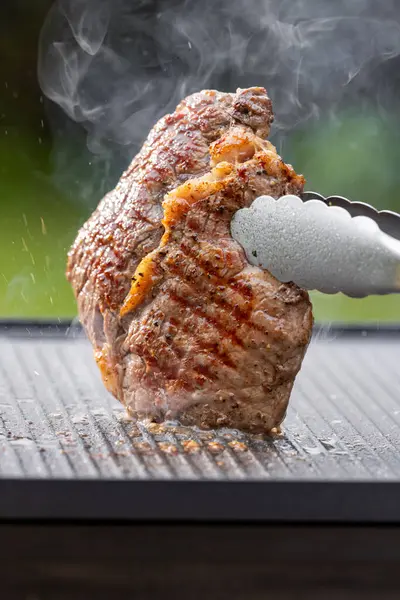 Sıcak elektrikli ızgara yüzeyinde tuzlu ve biberli taze ızgara biftek.